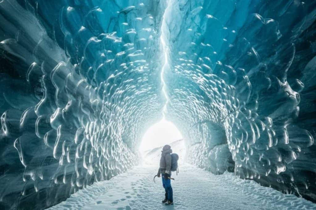 Traveler exploring a glowing blue ice cave in Alaska’s Mendenhall Glacier during winter.
